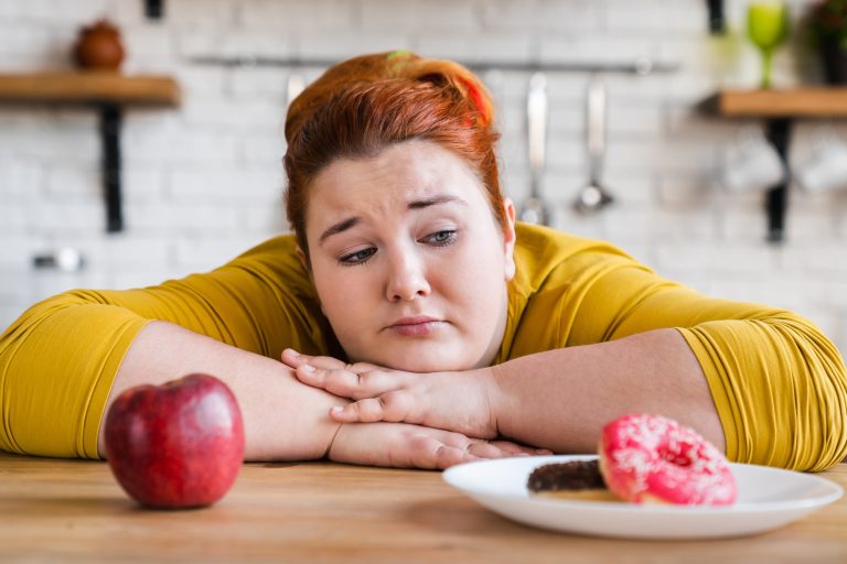Sad plump fat woman choosing between sweets and fruits, healthy eating and junk food. The choice.
