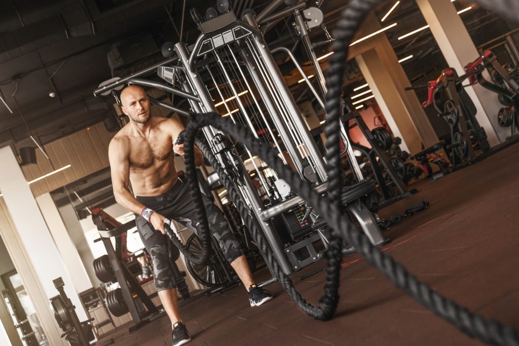 Handsome caucasian muscular man doing battle rope exercise while working out in gym