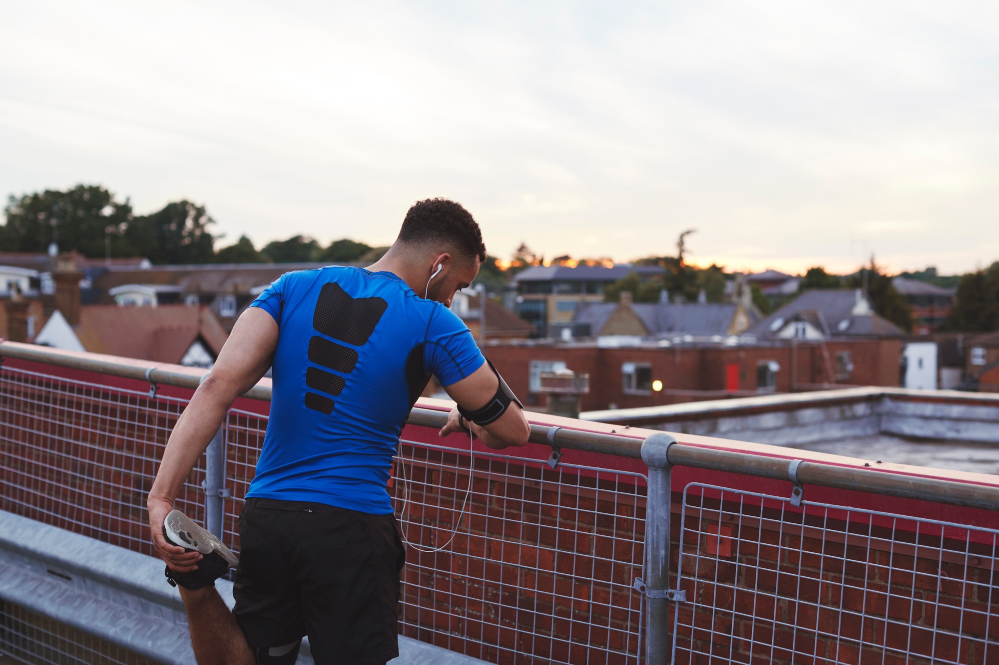 Male runner leaning on fence stretching leg in urban setting