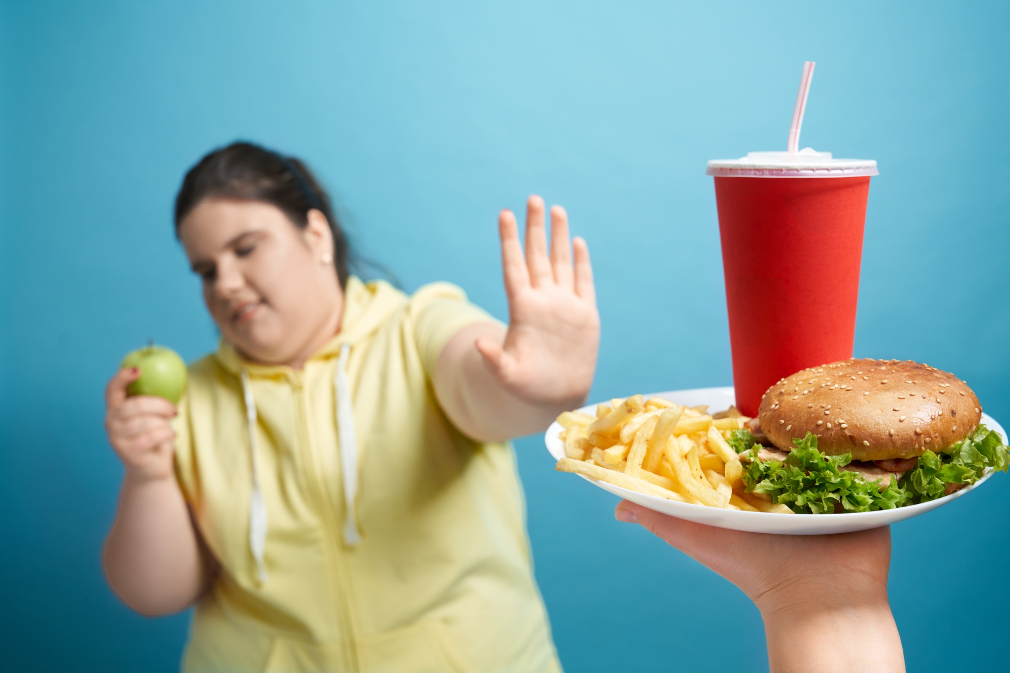 Portrait of fat lady pushing out plate with fastfood