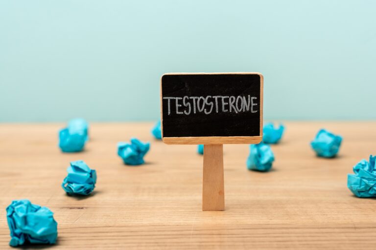 Nameplate with testosterone lettering near crumpled paper on wooden surface isolated on blue