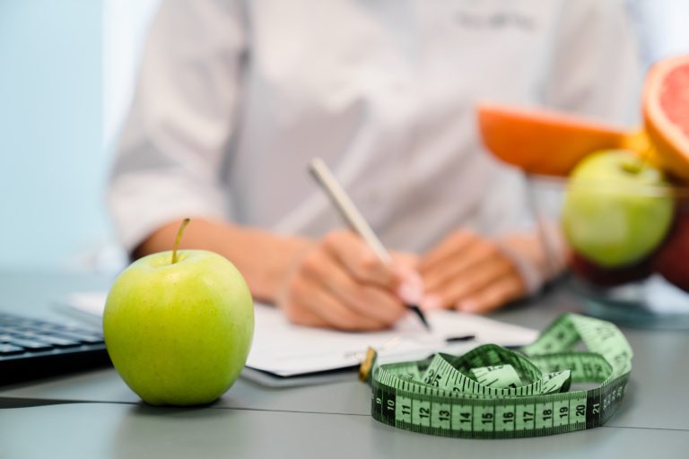 Nutritionist desk with fruits measuring tape, dietitian working on diet plan for overweight patient